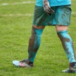 Keeper met Adidas keepershandschoenen duikt naar de bal tijdens een voetbalwedstrijd