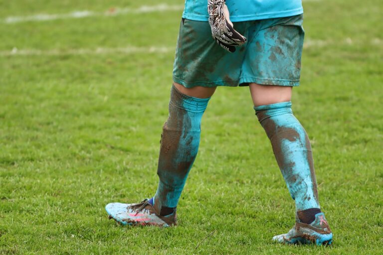 Keeper met Adidas keepershandschoenen duikt naar de bal tijdens een voetbalwedstrijd